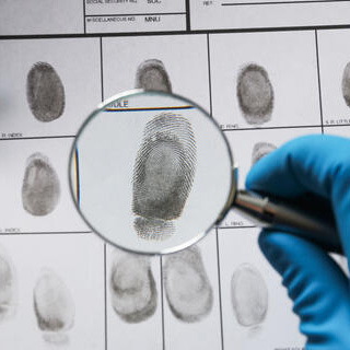 The image shows a criminal fingerprint record sheet being examined with a magnifying glass.