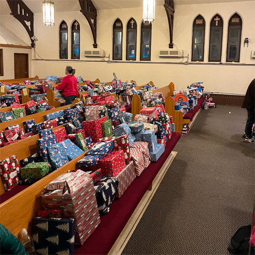 This image shows a holiday toy drive hosted inside a church, where volunteers are organizing gifts on the pews